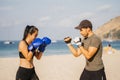 Asian woman and European man train boxing on a tropical beach. Personal training