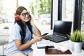 Asian woman with eyeglass using a mobile phone and headphones with a laptop and a notebook with a cup of coffee on the table Royalty Free Stock Photo