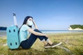 Asian woman with a face mask sitting with a suitcase