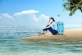 Asian woman with a face mask sitting with a suitcase on the beach