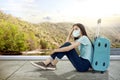 Asian woman with a face mask sitting with a suitcase