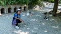 Asian woman with fedora and sunglasses kneeling in front of ducks and geese and looking at photographer Royalty Free Stock Photo