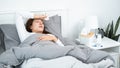 Asian woman feeling sick and sleeping in blanket on the bed while holding tissue in hand and touching forehead