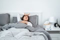 Asian woman feeling sick and sleeping in blanket on the bed while holding tissue in hand and touching forehead