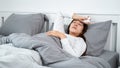 Asian woman feeling sick and sleeping in blanket on the bed while holding tissue in hands and touching forehead