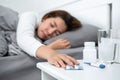 Asian woman feeling sick and using hands to touching pills on the table while lying in blanket on the bed