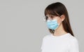 Asian woman feeling unwell and wearing face protective mask on grey studio background. Royalty Free Stock Photo