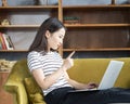 Asian woman finger wagging looking at laptop, working at home, liying on sofa