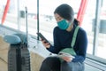 Asian woman flying in covid19 times - young tired and attractive Chinese girl in face mask waiting on airport checking mobile Royalty Free Stock Photo