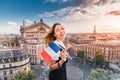 Asian woman with french flag and backpack standing on a roof top and enjoys great view over Parisian skyline at sunset. Royalty Free Stock Photo