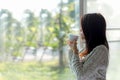 Asian woman fresh morning drinking coffee and looking out of the window on sunny day.