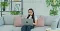 Asian woman in glasses sit on couch wear headset use laptop having distant communication. Telework provide support to