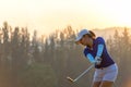 Asian woman golf player doing golf swing tee off on the green sunset evening time, Royalty Free Stock Photo