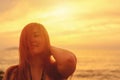 Woman with hair flowing down her face smiling at beach on sunset.