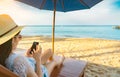 Asian woman with hat sit on sunbed under beach umbrella at sand beach and using smartphone on summer vacation. Girl in casual Royalty Free Stock Photo