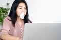 Asian woman having allergic rhinitis because of cold weather and dust sitting at office desk with tissue in her nose
