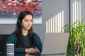 Asian woman having a business call in headphones at a desk, working on laptop in home office Royalty Free Stock Photo