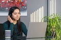 Asian woman having a business call in headphones at a desk, working on laptop in home office Royalty Free Stock Photo