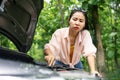 Unhappy Asian woman looking at opened hood broken car having problem with damaged engines