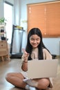 Asian woman having video call with laptop computer while sitting on floor in living room. Royalty Free Stock Photo