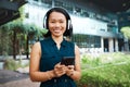 Asian woman, headphones and phone while streaming music, videos or podcast standing outside on break feeling free and Royalty Free Stock Photo