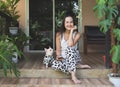 Asian woman and her chihuahua dog wearing dalmatian pattern costume sitting on balcony with house plants, smiling and looking at Royalty Free Stock Photo