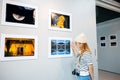 Asian woman hold camera at art gallery collection in front framed paintings Royalty Free Stock Photo