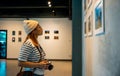 Asian woman hold camera at art gallery collection in front framed paintings pictures Royalty Free Stock Photo