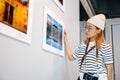 Asian woman hold camera at art gallery collection in front framed paintings pictures Royalty Free Stock Photo