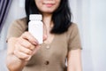 Asian woman holding a blank white squeeze bottle plastic tube for pills, capsules, or supplements. mockup