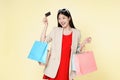 Asian woman holding credit card carry shopping bags isolated over light cream background. Smiling young girl purchasing online Royalty Free Stock Photo