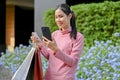 Asian woman holding credit card, using smartphone, carrying shopping bags Royalty Free Stock Photo