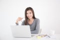 Asian woman holding glasses in hand and using laptop,Female smiling happily working in a white office desk Royalty Free Stock Photo