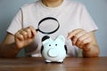 Asian woman holding magnifying glass in hand looking some thing on piggy bank, saving money concept Royalty Free Stock Photo