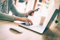 Asian woman holding phone and using computer laptop on wooden table Royalty Free Stock Photo