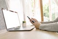 Asian woman holding phone and using computer laptop on wooden table Royalty Free Stock Photo