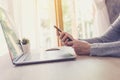 Asian woman holding phone and using computer laptop on wooden table Royalty Free Stock Photo