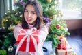 Asian woman holding red gift box on the hands offer to you on christmas tree background