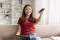 Asian woman holding remote control and digital tablet while sitting on couch Royalty Free Stock Photo