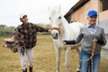 Asian woman holding saddle while older woman rancher leading horse outdoors Royalty Free Stock Photo