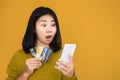 Asian woman holding smart phone and credit card shocked with overspending money from shopping online