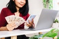 Asian woman holding Thai money using smart phone and laptop on desk, register, paying online concept Royalty Free Stock Photo