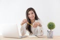 Asian woman holding yellow pencil in hand and using laptop,Female smiling happily working in a white office desk Royalty Free Stock Photo