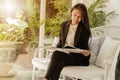 Asian woman at home sitting near window relaxing in her living room reading book. Beautiful gril wearing black suit sitting Royalty Free Stock Photo