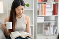 Asian woman at home sitting and reading a book on the sofa in the living room Smiling young woman relaxing in her living room Royalty Free Stock Photo