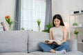 Asian woman at home sitting and reading a book on the sofa in the living room. Young woman relaxing in the living room of her home Royalty Free Stock Photo