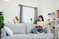 Asian woman at home sitting and reading a book on the sofa in the living room. Young woman relaxing in the living room of her home Royalty Free Stock Photo