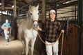 Asian woman horse breeder leading white thoroughbred racehorse in stable Royalty Free Stock Photo