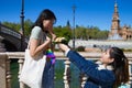 Asian woman kneeling giving a bouquet of roses to her little sister. In the background a large square. The girl receiving the