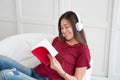 Asian woman listening music on headphone and reading book with relax pose at couch in living room at home.leisure lifestyle Royalty Free Stock Photo